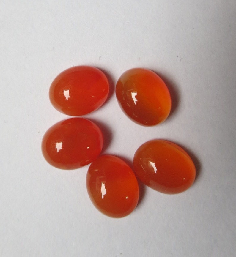 May include: Five oval-shaped carnelian gemstones in various shades of orange. The stones are smooth and polished, with a glossy finish.
