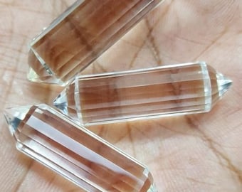May include: Three clear quartz crystal points, also known as wands, with a slight brown hue. The points are lying on a hand.
