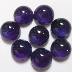 May include: Eight round, polished amethyst cabochons in various shades of purple. The cabochons are arranged in a circular pattern on a white surface.
