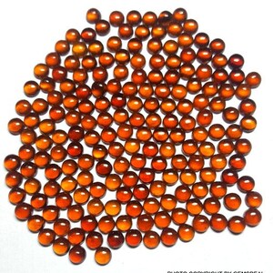 May include: A large group of small, round, orange-brown gemstones. The gemstones are arranged in a circular pattern, with the largest gemstone in the center.