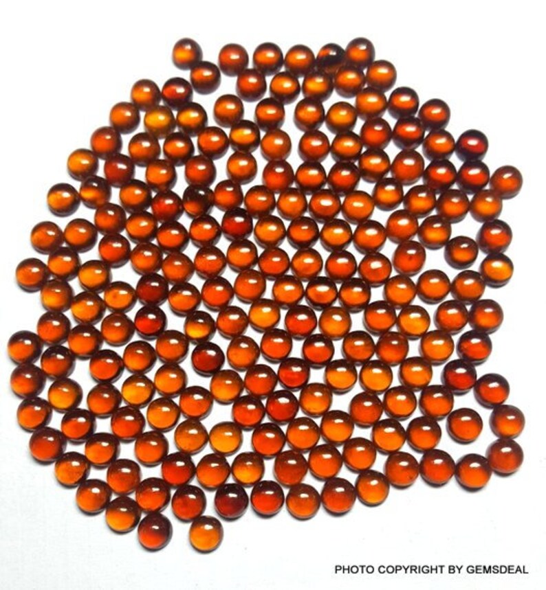 May include: A large group of small, round, orange-brown gemstones. The gemstones are arranged in a circular pattern, with the largest gemstone in the center.