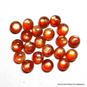 May include: A collection of 18 round, orange sunstone cabochons. The stones have a shimmery, iridescent finish.