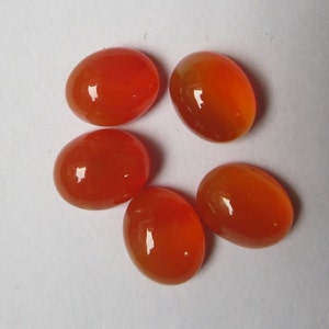 May include: Five oval-shaped carnelian gemstones, each with a smooth, polished surface and a vibrant orange color.