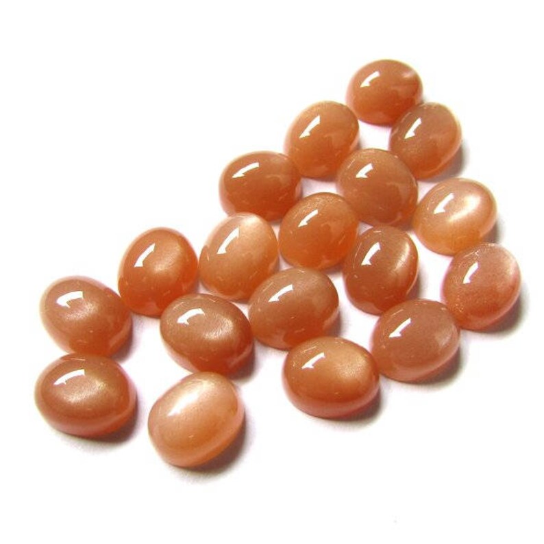 May include: A collection of 17 oval-shaped, orange sunstone cabochons. The stones have a smooth, polished surface and a subtle shimmer.