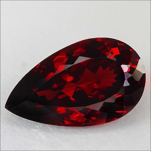 May include: A deep red pear-shaped gemstone with a faceted cut. The gemstone is set against a white background.