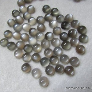 May include: A collection of 40 gray moonstone cabochons, each measuring approximately 10mm in diameter. The stones have a smooth, rounded surface and a subtle shimmer.