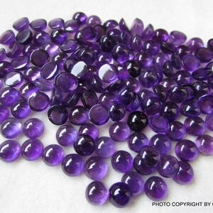 May include: A large group of round, purple amethyst cabochons. The cabochons are smooth and polished, with a slight sheen.