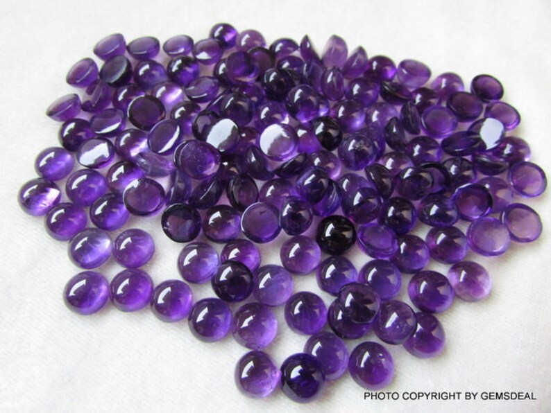 May include: A large group of round, purple amethyst cabochons. The cabochons are smooth and polished, with a slight sheen.