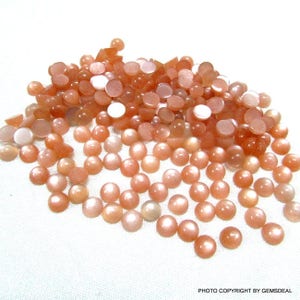 May include: A large pile of round, orange-colored sunstone cabochons. The stones have a shimmery, iridescent finish.