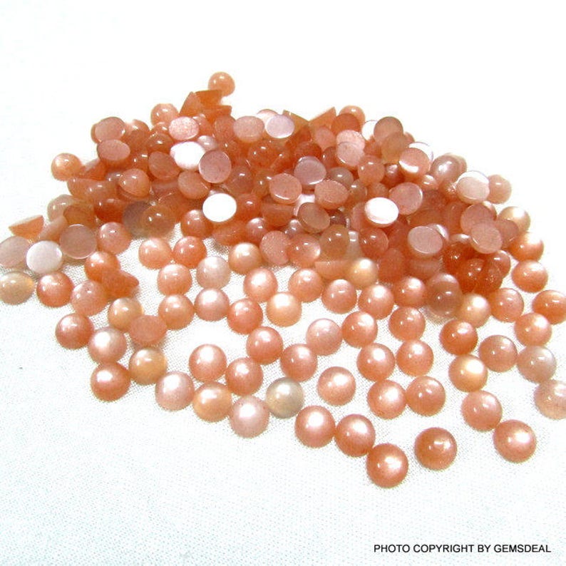 May include: A large pile of round, orange-colored sunstone cabochons. The stones have a shimmery, iridescent finish.