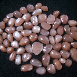 May include: A collection of approximately 50 loose, faceted, peach-colored sunstone gemstones. The stones are various sizes and shapes, with a pearlescent sheen.