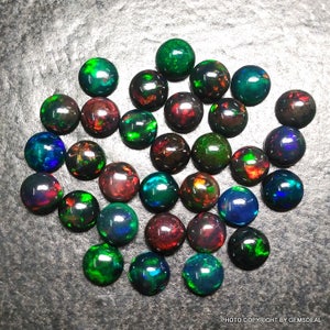 May include: A collection of 25 round black opal cabochons, each displaying a variety of iridescent colors, including green, blue, red, and orange.