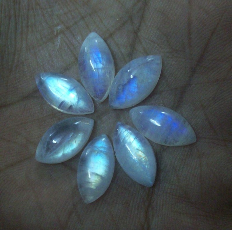 Puede incluir: Siete cabujones de piedra lunar iridiscente en forma de marquesa, dispuestos en forma de flor en una mano.