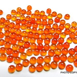 May include: A large group of round, orange and yellow cabochon gemstones. The stones are smooth and polished, with a slight sheen.