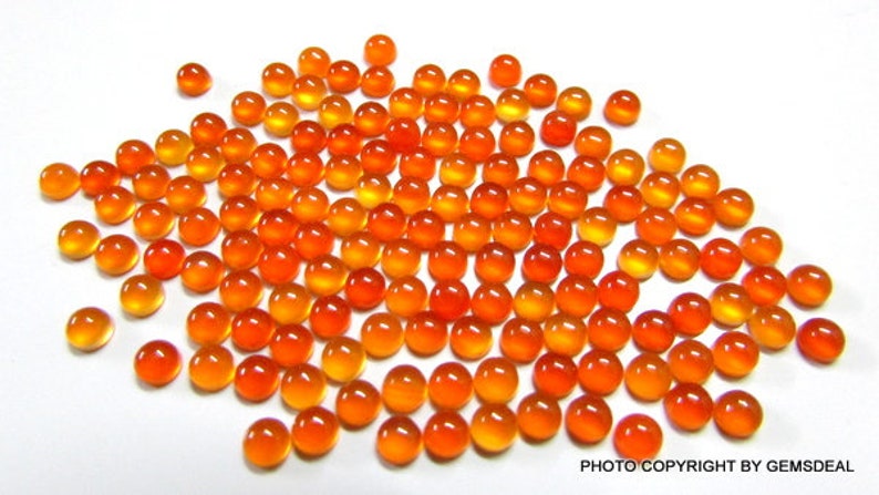 May include: A large group of round, orange and yellow cabochon gemstones. The stones are smooth and polished, with a slight sheen.