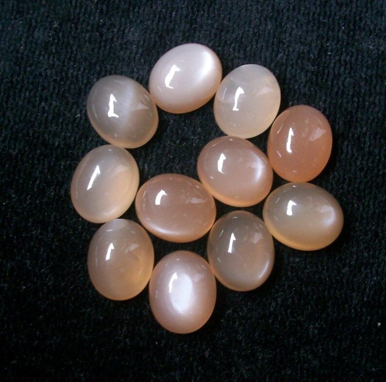 May include: A collection of ten oval-shaped moonstone cabochons in various shades of pink and white. The stones are smooth and polished, with a subtle shimmer.