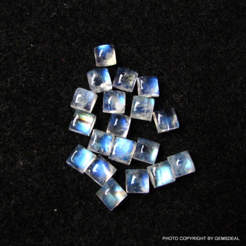K&ouml;nnte beinhalten: Eine Sammlung von 15 regenbogenfarbenen blauen Mondstein-Quadratcabochons, die jeweils etwa 6 mm x 6 mm messen. Die Steine ​​liegen lose auf einem schwarzen Hintergrund.