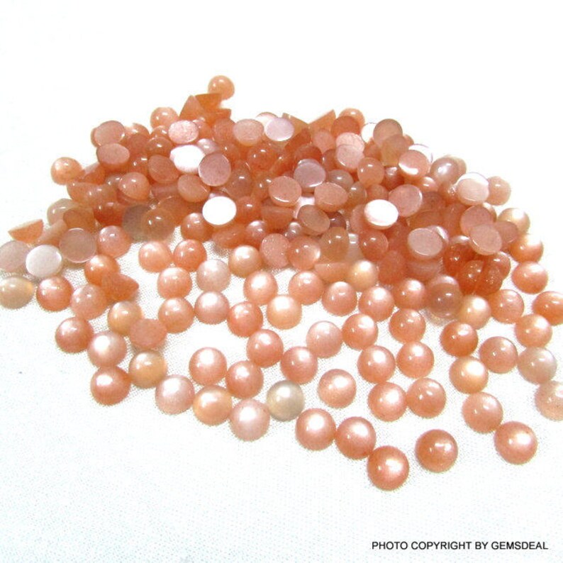 May include: A pile of round, peach-colored sunstone cabochons. The stones have a shimmery, iridescent finish.