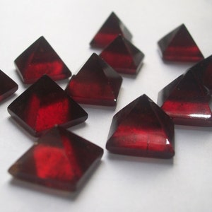 May include: A group of ten red gemstone pyramids, each with a smooth, polished surface. The pyramids are arranged in a random pattern on a white background.