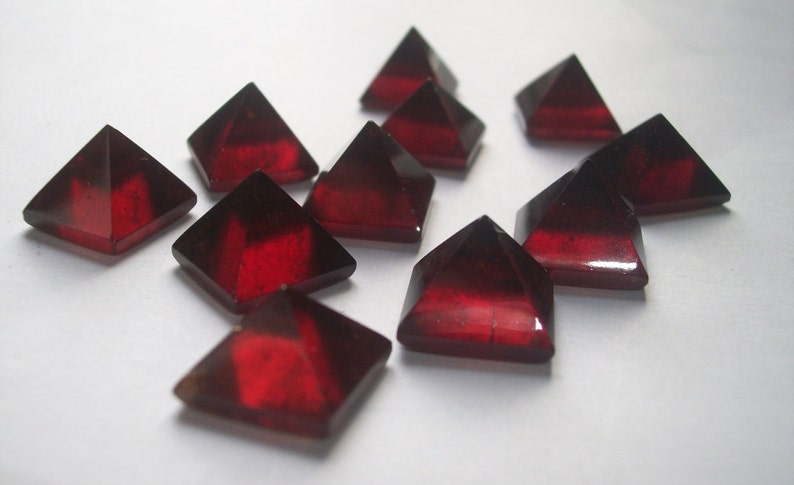 May include: A group of ten red gemstone pyramids, each with a smooth, polished surface. The pyramids are arranged in a random pattern on a white background.