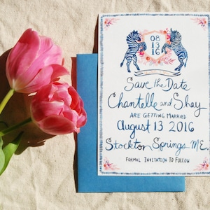 May include: Save the Date card featuring a watercolour illustration of two zebras in blue and white. The card is decorated with pink and blue flowers and includes the text "Save the Date Chantelle and Shay Are Getting Married August 13 2016 Stockton Springs ME Formal Invitation to Follow."