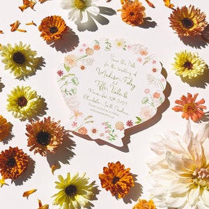 May include: Save the Date card featuring a floral design in the shape of a seashell. The card is for the wedding of Madison Foley and Tiffer Valente on 10th November 2023 in Charleston, South Carolina. The text "madisonandtiffer.com" is printed at the bottom of the card.