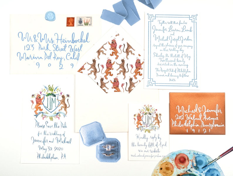 May include: Save the date card featuring a watercolour illustration of a lion and cheetah with a crest displaying the initials "JM". The card is adorned with flowers and foliage. The text reads "Please Save the Date for the wedding of Jennifer and Michael May 30, 2020 Philadelphia, PA"
