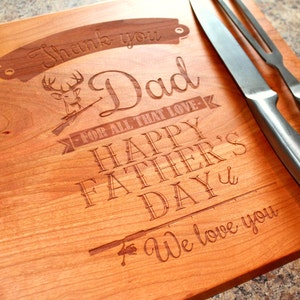 May include: A wooden cutting board with a laser engraved message that reads "Thank you Dad for all that love - Happy Father's Day - We love you". The board features a deer with antlers and a fishing rod.