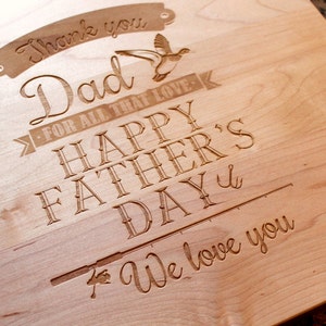 May include: A wooden cutting board with an engraved message that reads "Thank you Dad - For all that love - Happy Father's Day - We love you". The message is surrounded by a decorative border and includes a small image of a bird.