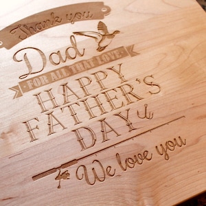 May include: A wooden cutting board with an engraved message that reads "Thank you Dad - For all that love - Happy Father's Day - We love you". The message is surrounded by a decorative border and includes a small image of a bird.