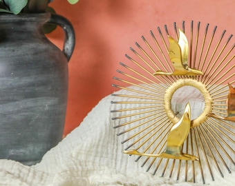 May include: Gold metal wall art featuring three stylized birds in flight against a sunburst background. The birds are made of metal and have a shiny finish.