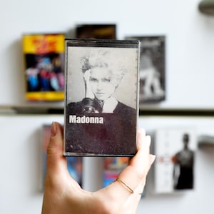 May include: A cassette tape with a black and white photo of Madonna on the front. The tape is labeled "Madonna" in white text.