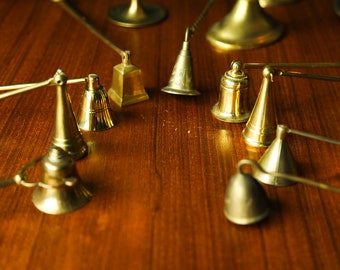 May include: A collection of antique brass candle snuffers with long handles. The snuffers are arranged on a wooden surface.