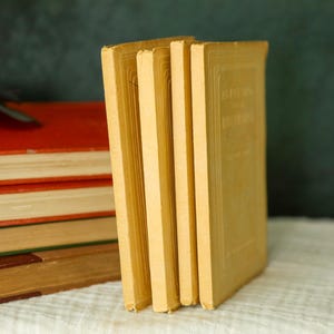 May include: A stack of three upright yellow books with textured covers standing next to a horizontal pile of four books with red, brown, and green covers. The yellow books feature embossed rectangular borders on their front covers.