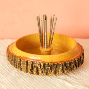 May include: A wooden nut bowl with a natural bark edge and a light yellow interior. The bowl holds a set of silver nutcrackers. The background is a soft peach color.