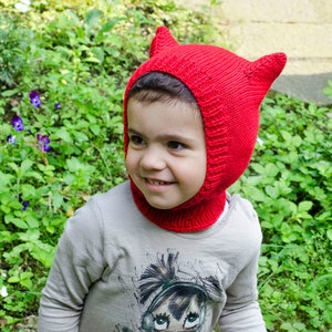 The image features a three-year-old girl wearing a red balaclava with cat ears. The balaclava covers ears, throat and neck.
