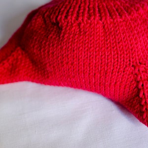 May include: A close-up of a bright red knitted pillow with a textured surface.