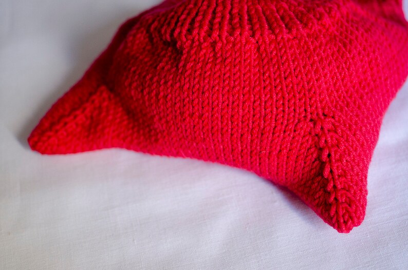 May include: A close-up of a bright red knitted pillow with a textured surface.