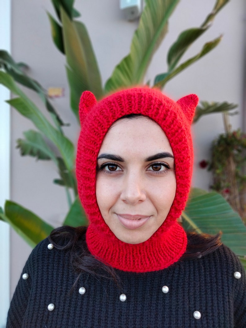 The image features a young woman wearing a red balaclava with cat ears. The balaclava covers ears, throat and neck.