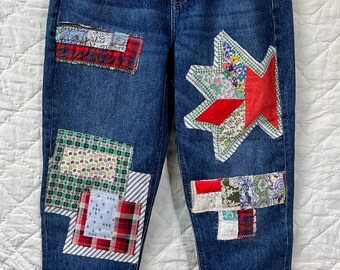 May include: Blue denim jeans with patchwork details. Patches include red, white, and patterned fabrics in various shapes. The jeans have a straight leg and the brand "AMERICAN EAGLE" is visible.