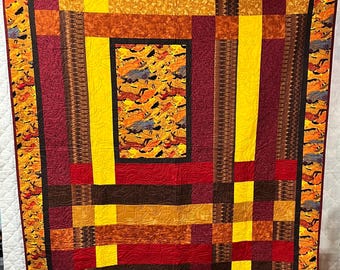 May include: A handmade quilt with a patchwork design. The quilt features a mix of warm colors, including yellow, red, and brown. The border has a pattern of leaves. The quilt is likely made of cotton and is suitable for a bed or as a decorative item.