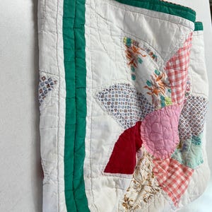 May include: A quilted tote bag featuring a patchwork floral design in shades of pink, red, and white with green fabric borders. The bag is constructed from various patterned fabric pieces and includes two beige fabric handles at the top.