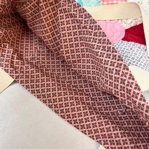 May include: A tote bag featuring a pink and brown geometric patterned fabric lining. The exterior is constructed from a patchwork quilt design with various colors and textures, including red velvet and light blue fabric, with cream-colored straps.