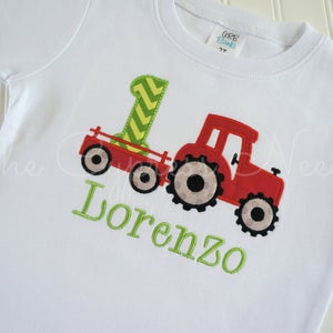 May include: White t-shirt with a red tractor and a green number one on it. The name Lorenzo is embroidered in green below the tractor.