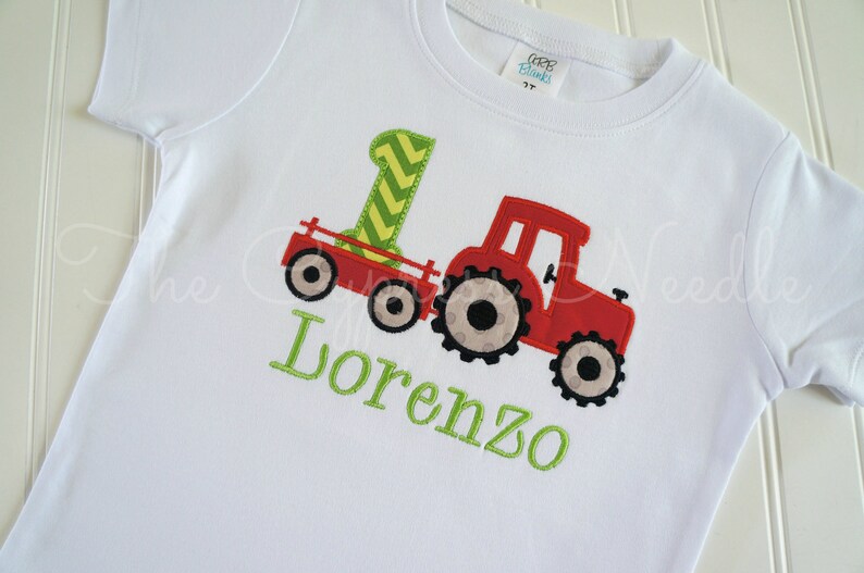 May include: White t-shirt with a red tractor and a green number one on it. The name Lorenzo is embroidered in green below the tractor.