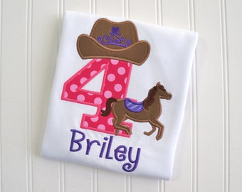 May include: A white t-shirt with a pink polka dot number four, a brown cowboy hat with a purple crown, a brown horse with a purple saddle, and the name "Briley" embroidered in purple.