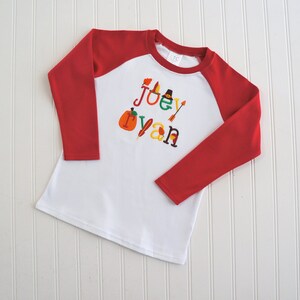 Puede incluir: Camiseta de b&eacute;isbol de manga larga blanca con mangas rojas. La camiseta tiene un dise&ntilde;o de tem&aacute;tica de Acci&oacute;n de Gracias con el nombre "Joey Ryan" escrito en letras de colores y decorado con iconos de tem&aacute;tica oto&ntilde;al.