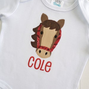 May include: White baby onesie with a brown and red horse applique and the name "COLE" embroidered in red.