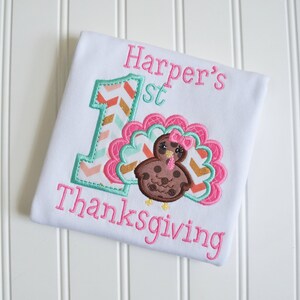 May include: A white onesie with pink and green embroidery. The onesie says "Harper's 1st Thanksgiving" with a number one and a turkey.