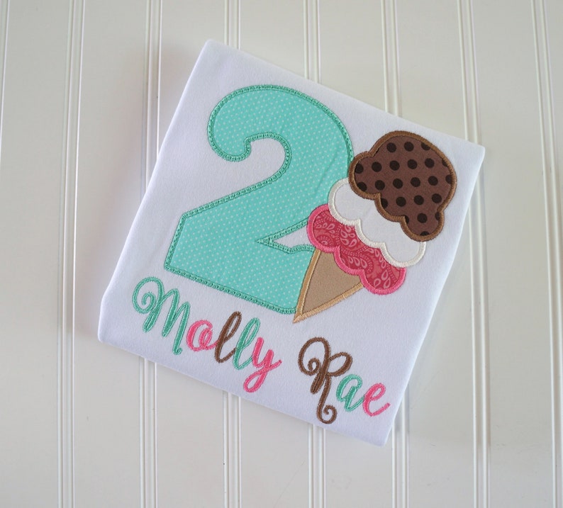 May include: A white t-shirt with a turquoise number two, a brown and pink ice cream cone, and the name "Molly Rae" embroidered in brown and pink.